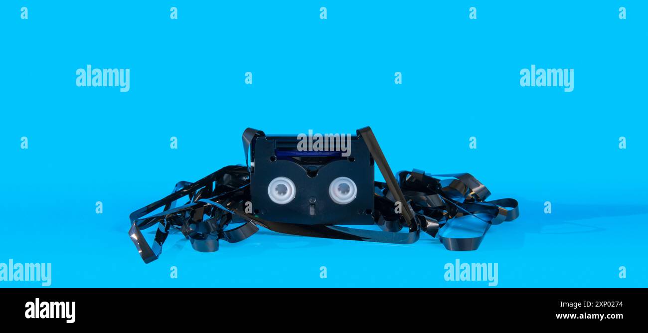 Ancienne mini cassette DV noire endommagée avec la bande extérieure entourant la cassette sur fond bleu Banque D'Images