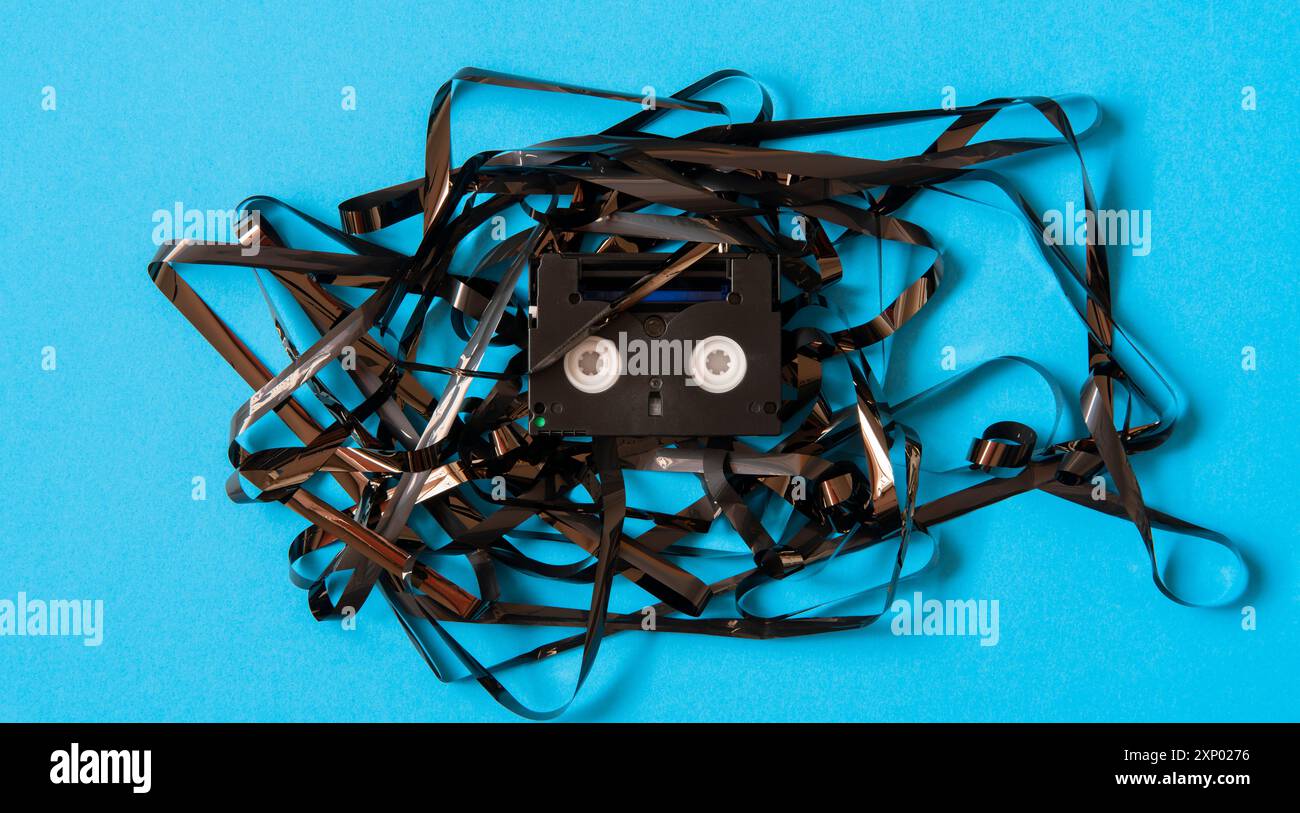 Ancienne mini cassette DV noire avec bande enchevêtrée entourant la cassette sur fond bleu Banque D'Images