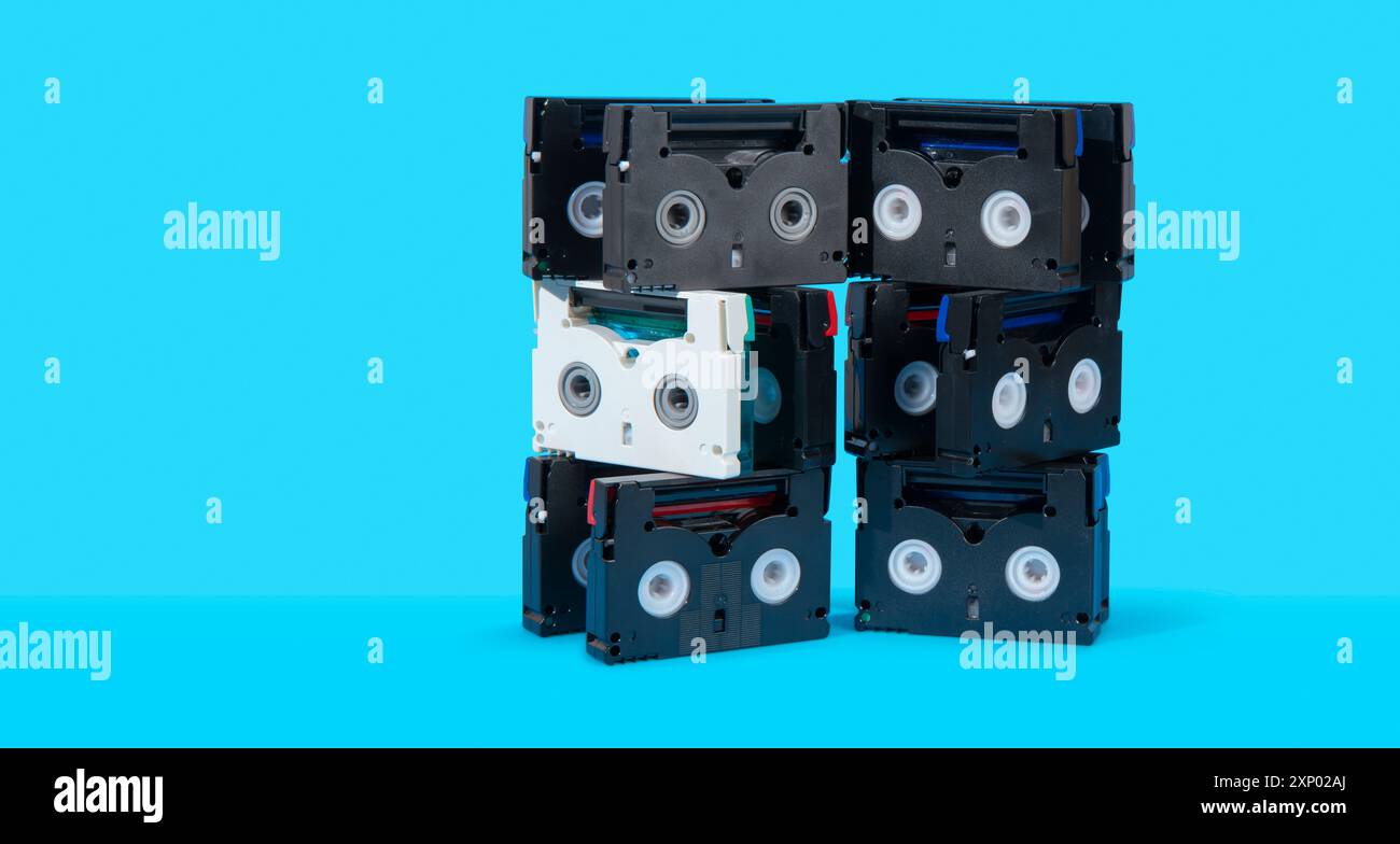Vue avant d'une tour de vieilles mini cassettes DV noires sur une surface bleue sur fond bleu Banque D'Images