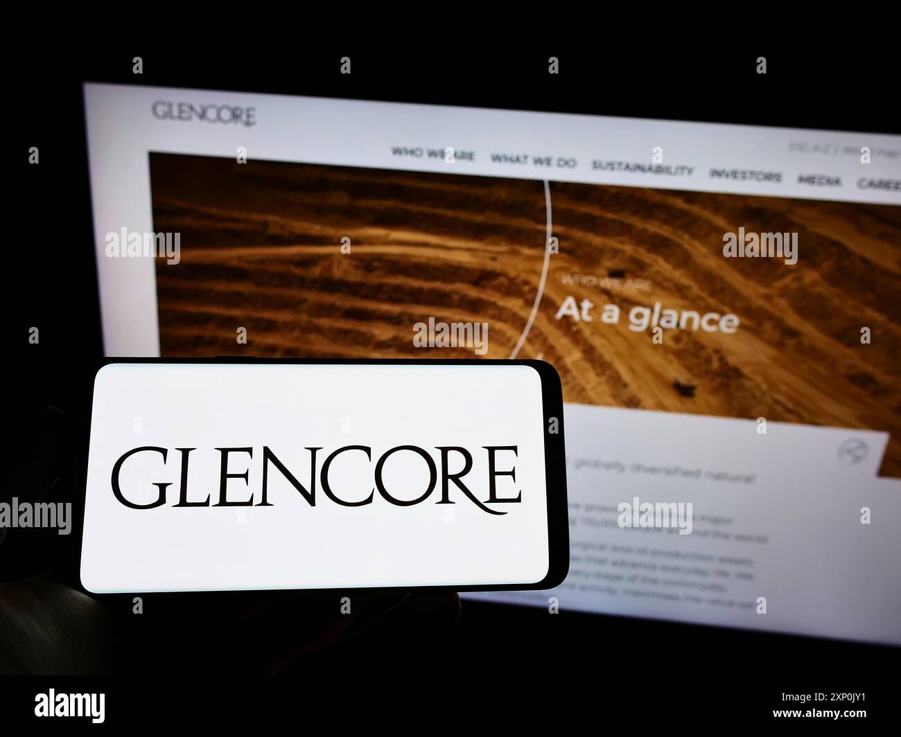 Stuttgart, Allemagne, 01-28-2022, personne tenant le téléphone portable avec le logo de la société de négoce de marchandises Glencore plc sur l'écran en face de la page Web d'affaires. Banque D'Images