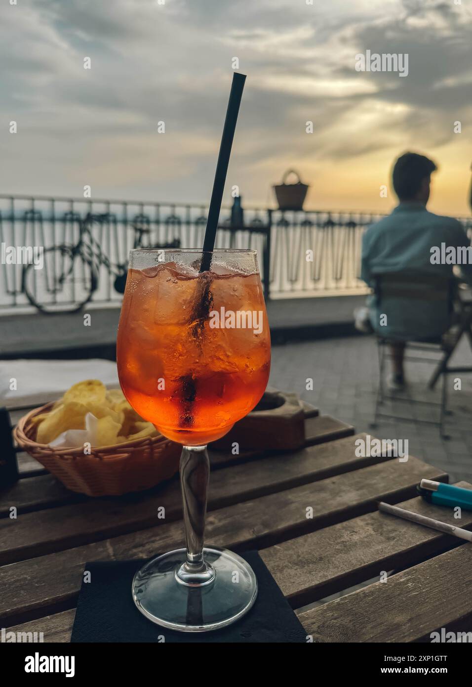 Un verre de vin rouge avec une paille est assis sur une table à côté d'un panier de frites. La scène se déroule sur une table en bois à l'extérieur, avec une personne assise dedans Banque D'Images