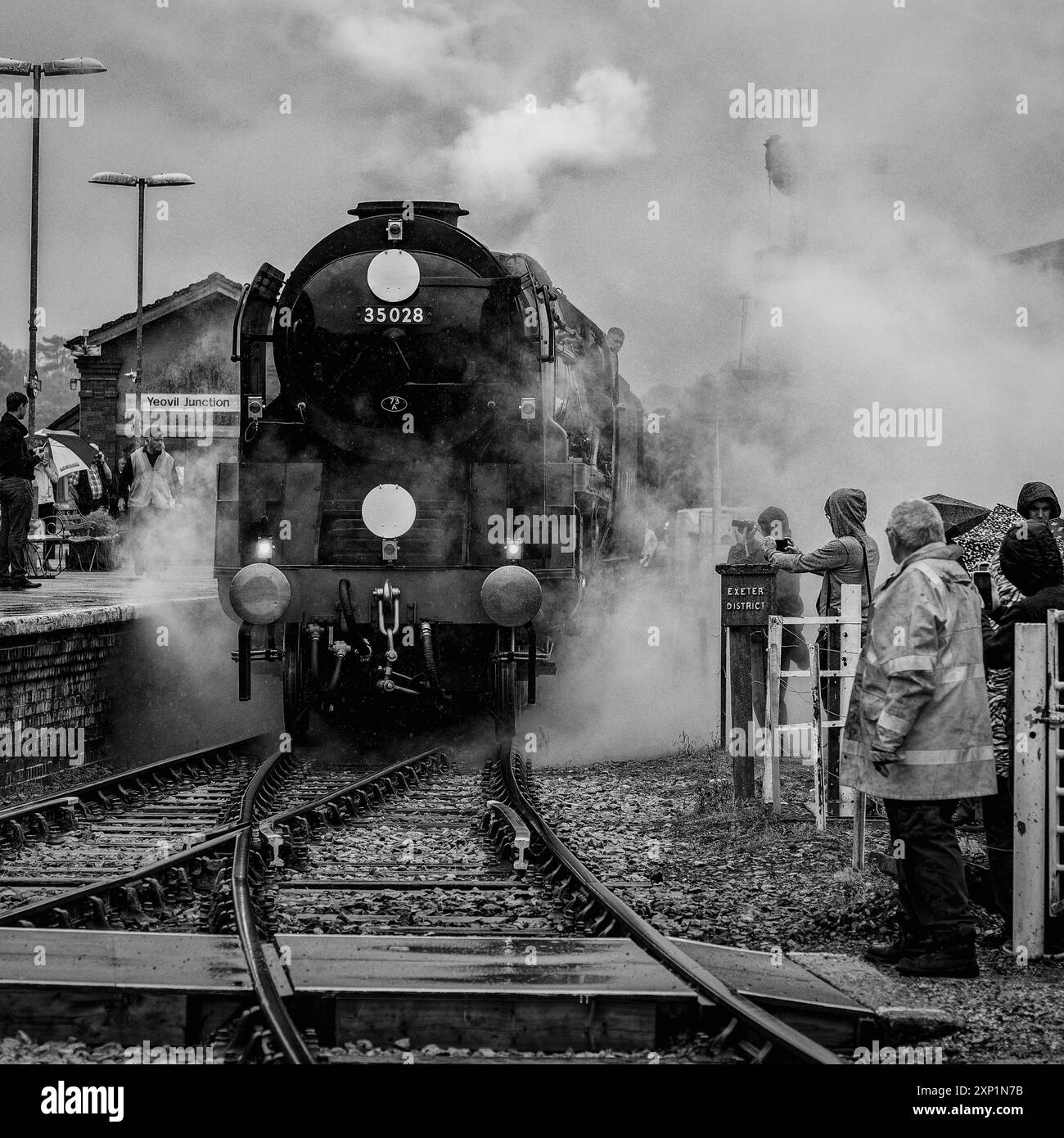 Une locomotive à vapeur d'époque, la 35028 Clan Line, s'approche de la gare avec de la fumée qui s'échappe de sa cheminée et un conducteur qui branle de la cabine Banque D'Images