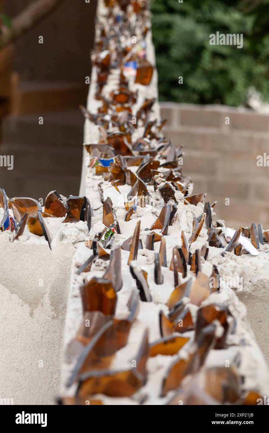 Une photo détaillée de éclats de verre tranchants posés dans du béton sur un mur comme mesure de sécurité en Gambie, symbolisant la protection et les barrières. Banque D'Images