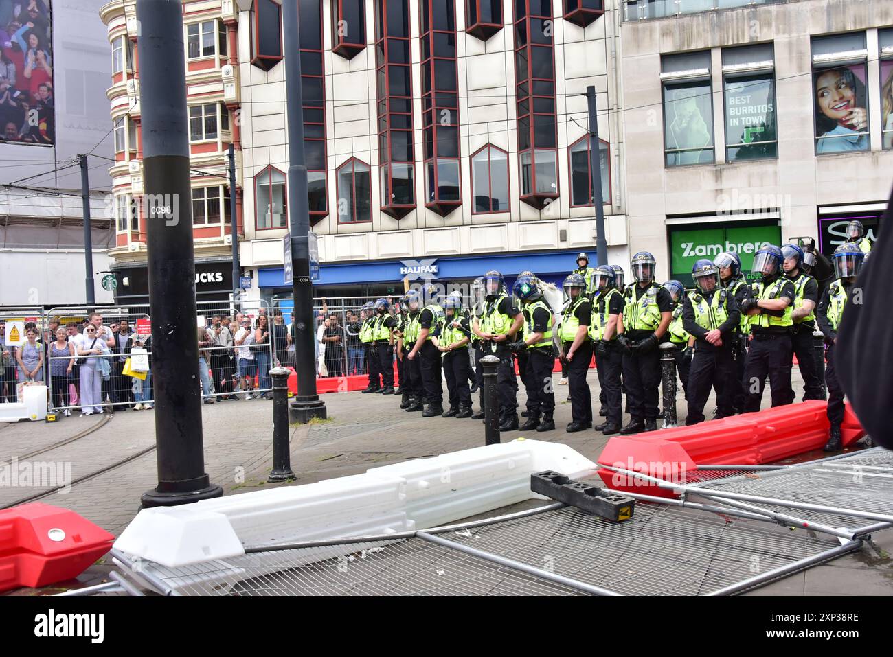 Manchester, Royaume-Uni, 3 août 2024. Tenez-vous debout entre la police anti-émeute portant des casques et les manifestants. Les manifestants ont démoli des clôtures autour des lignes de tramway. Parmi les manifestants figurent des partisans de la Ligue de défense anglaise et des antiracistes à Piccadilly Gardens, dans le centre de Manchester, au Royaume-Uni, à la suite de l'agression meurtrière de trois jeunes filles à Southport et des violentes émeutes qui ont suivi. La police était là en grand nombre. Crédit : Terry Waller/Alamy Live News Banque D'Images