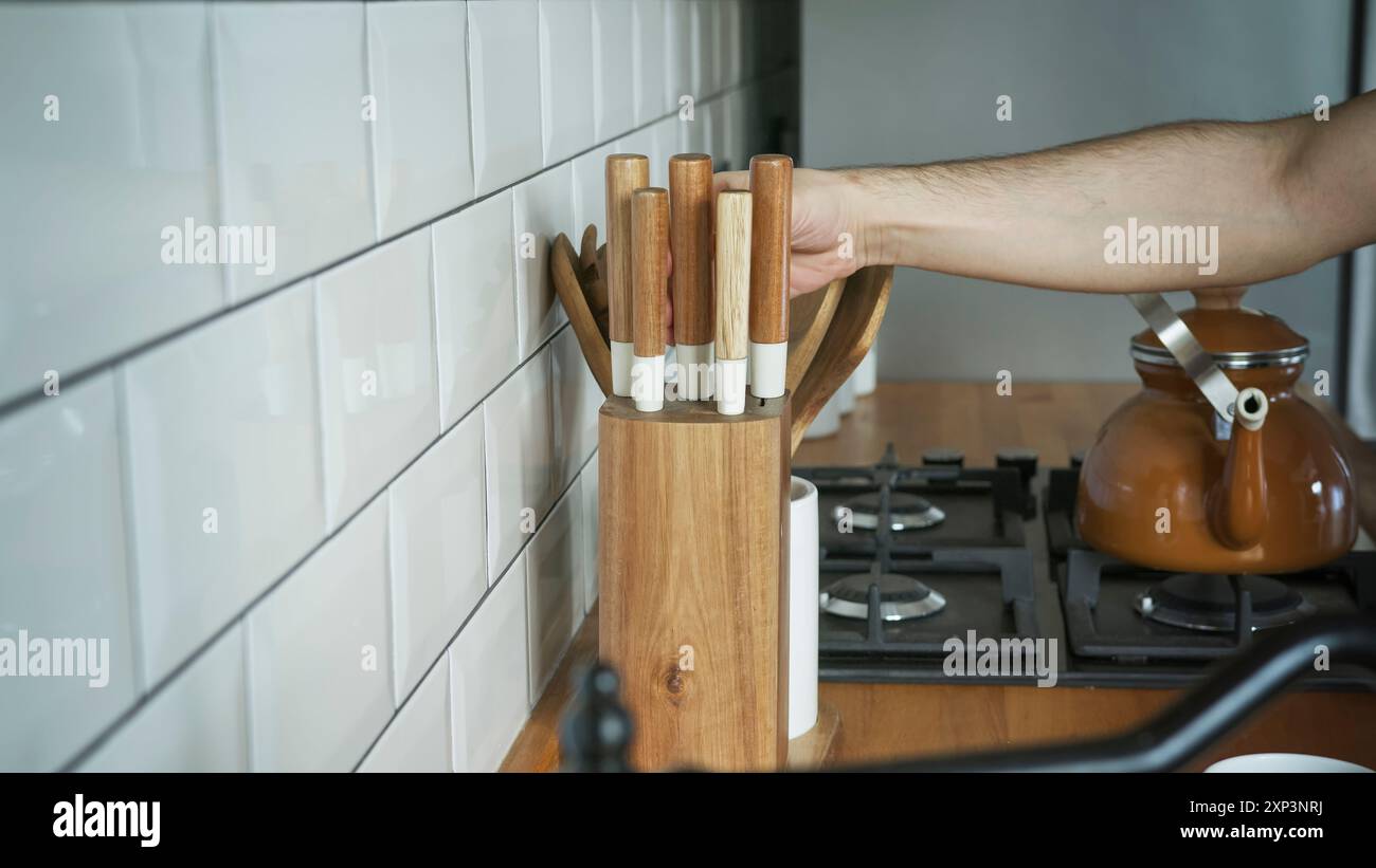 Une personne sélectionne un couteau à partir d'un bloc de couteaux en bois dans une cuisine moderne, la préparation culinaire et la cuisine maison. Outils de cuisine, routines de cuisine, a Banque D'Images