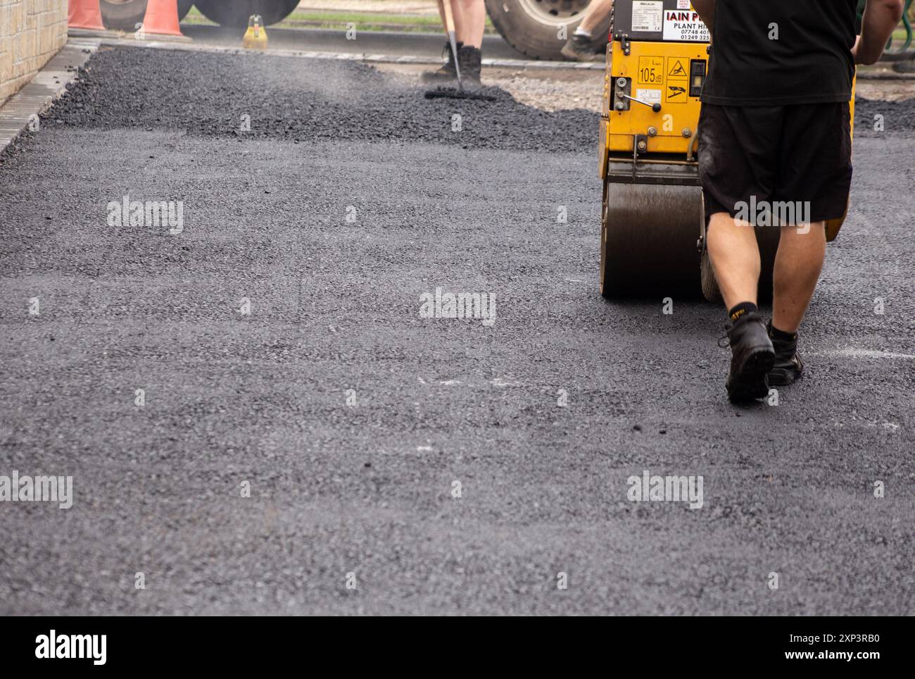 Ouvriers qui pavent une route asphaltée noire avec un compacteur à rouleaux et lissent l'asphalte frais avec un râteau. Banque D'Images