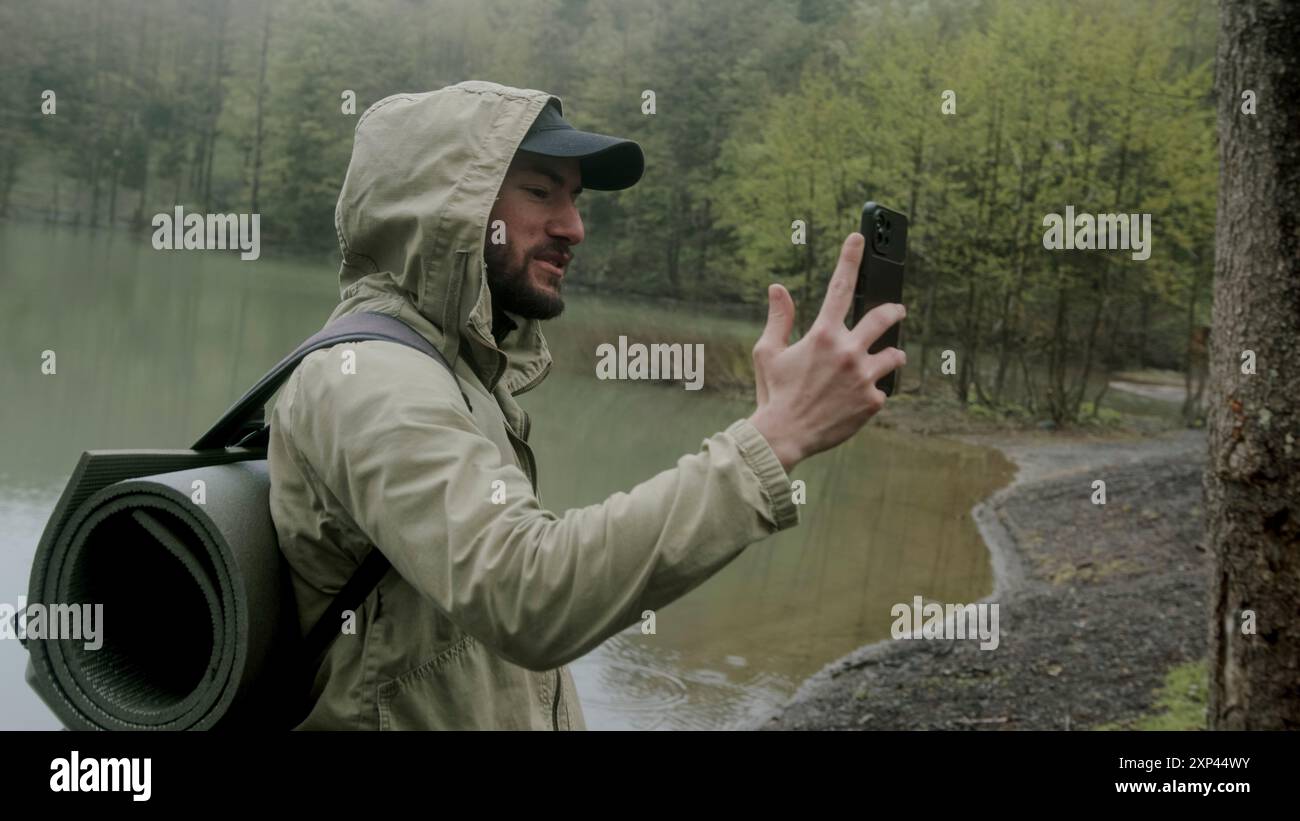 Aventureux randonneur homme passe un appel vidéo avec son téléphone portable dans la forêt. Banque D'Images