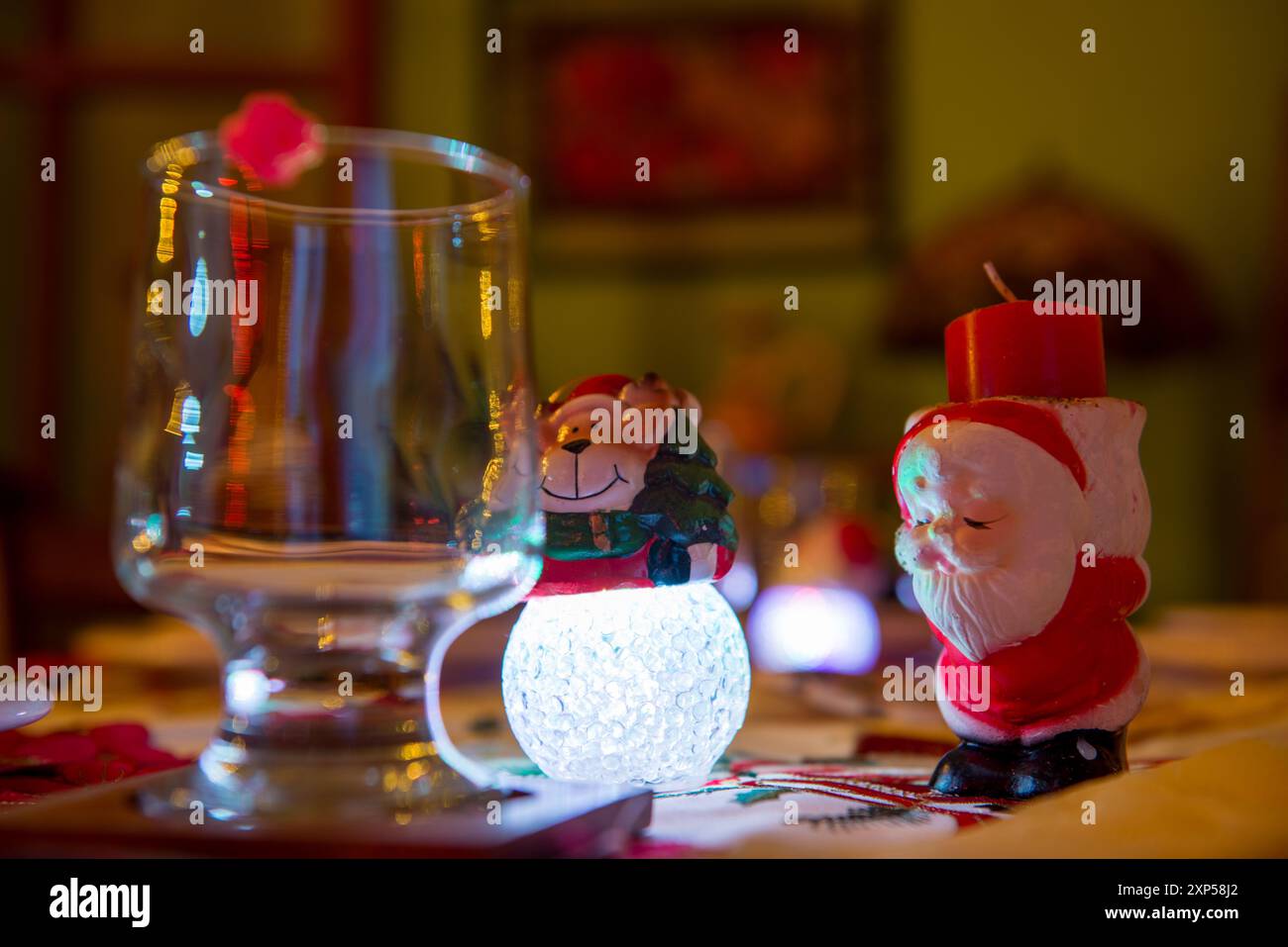 Table de Noël : bougie de Père Noël, lumière de bonhomme de neige, verre vide, ambiance chaleureuse Banque D'Images