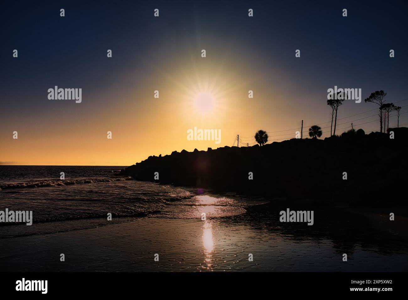 Coucher de soleil avec des rayons de lumière se reflétant sur le sable humide et Rock Jetty à Cape San Blas, Floride États-Unis Banque D'Images