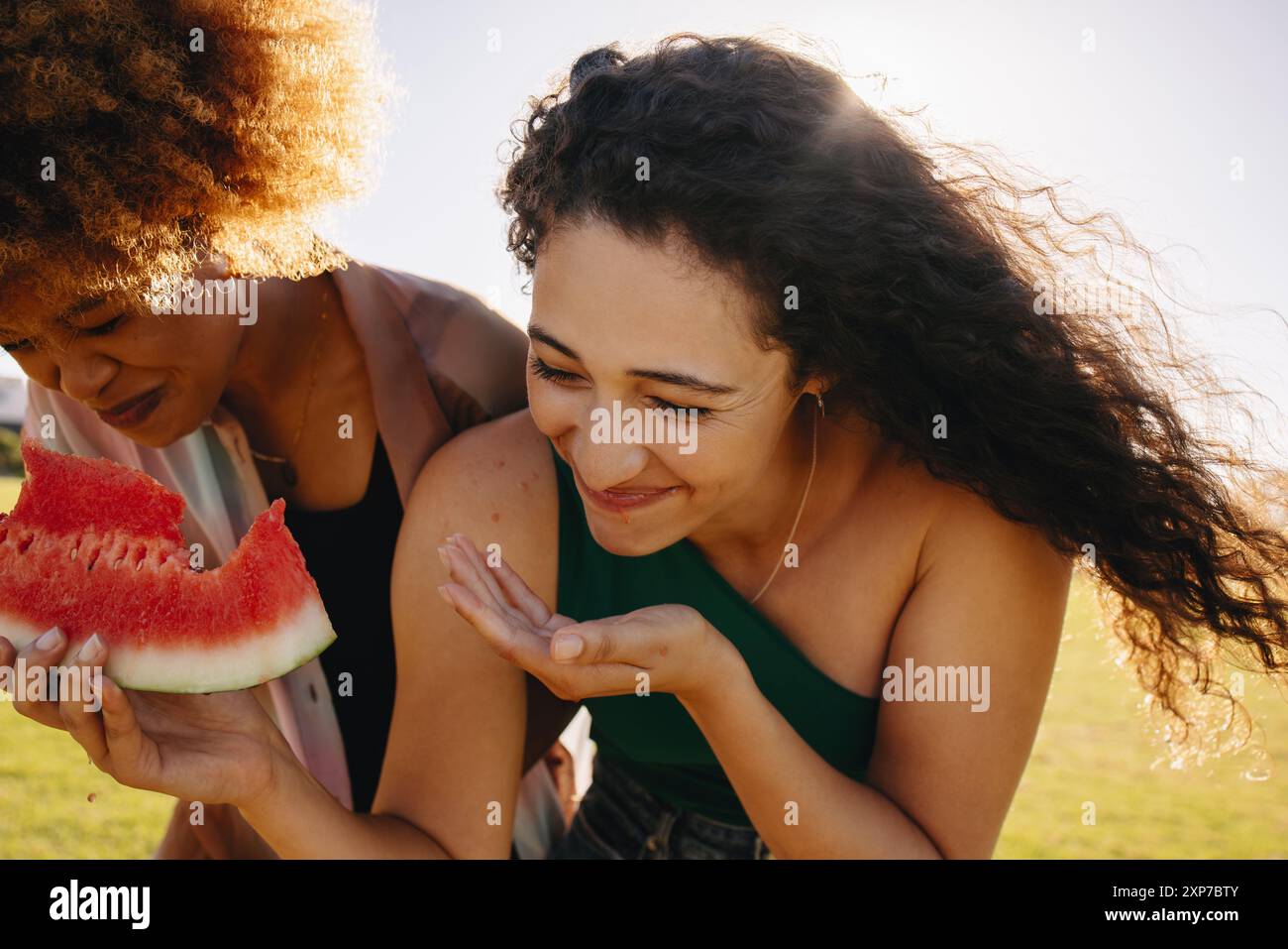 Meilleurs amis partageant des moments spéciaux et des rires tout en dégustant une délicieuse tranche de pastèque sur une pelouse de parc. Banque D'Images
