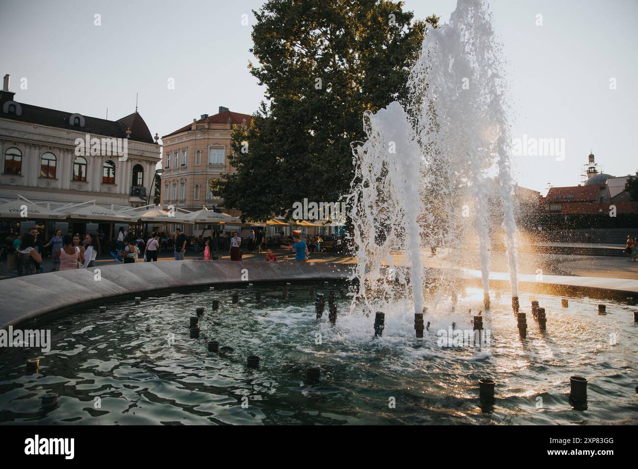 Une place animée de la ville avec une fontaine et les gens appréciant la soirée près des bâtiments historiques Banque D'Images