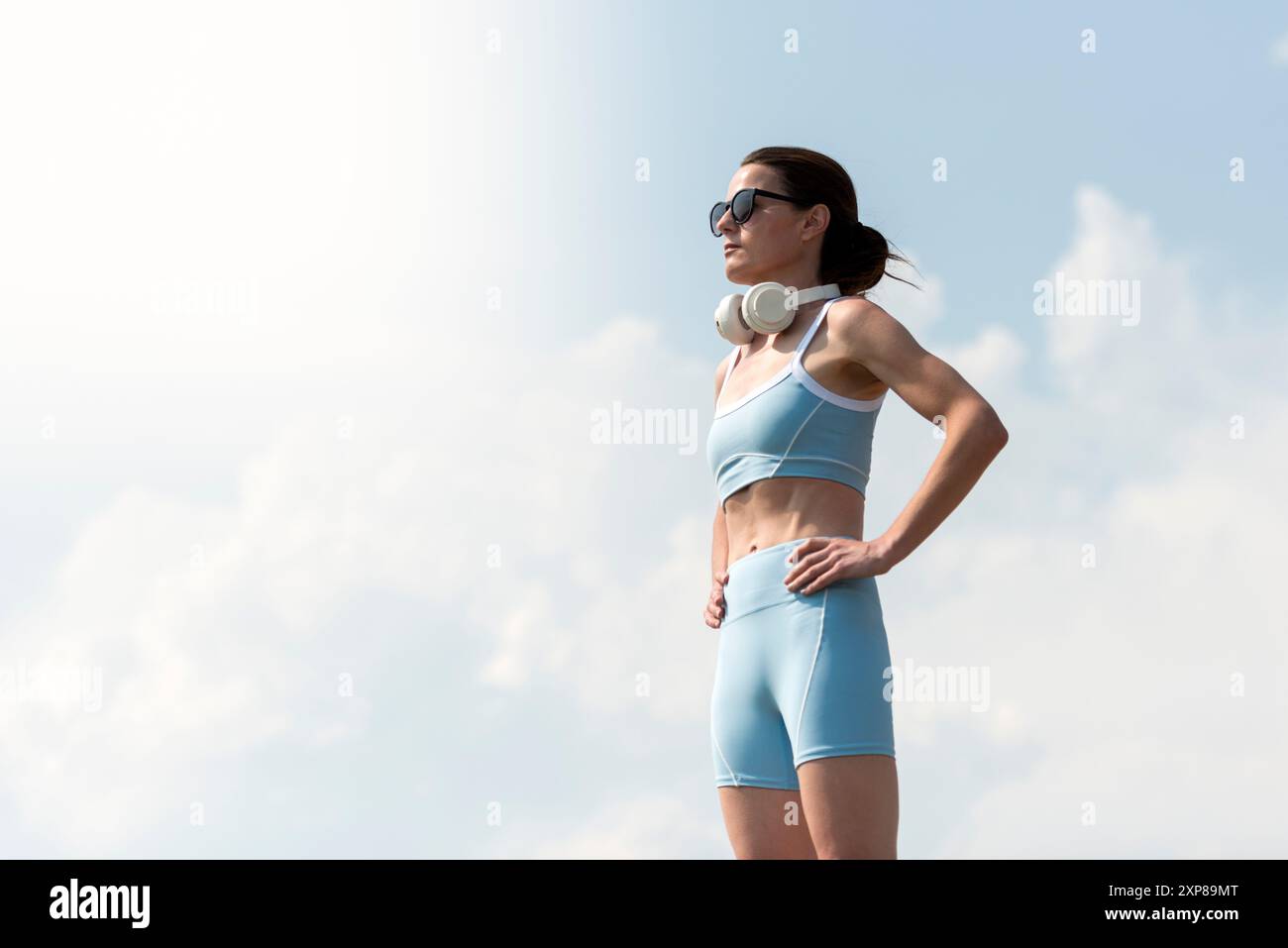 femme sportive debout avec les mains sur les hanches, écouteurs, à l'extérieur Banque D'Images femme sportive debout avec les mains sur les hanches, écouteurs, à l'extérieur Banque D'Images
