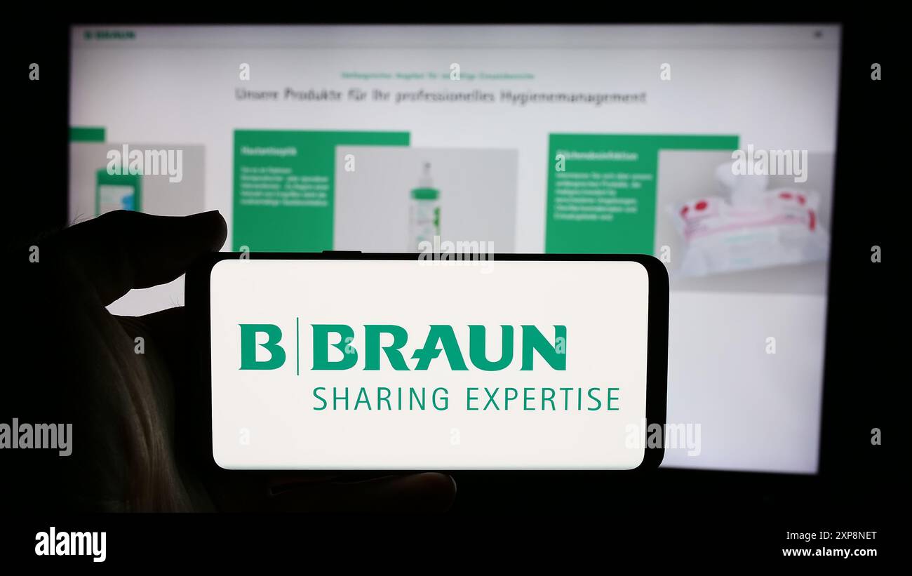 Personne tenant un téléphone portable avec le logo de la société allemande de dispositifs pharmaceutiques B. Braun se en face de la page Web de l'entreprise. Concentrez-vous sur l'affichage du téléphone. Banque D'Images