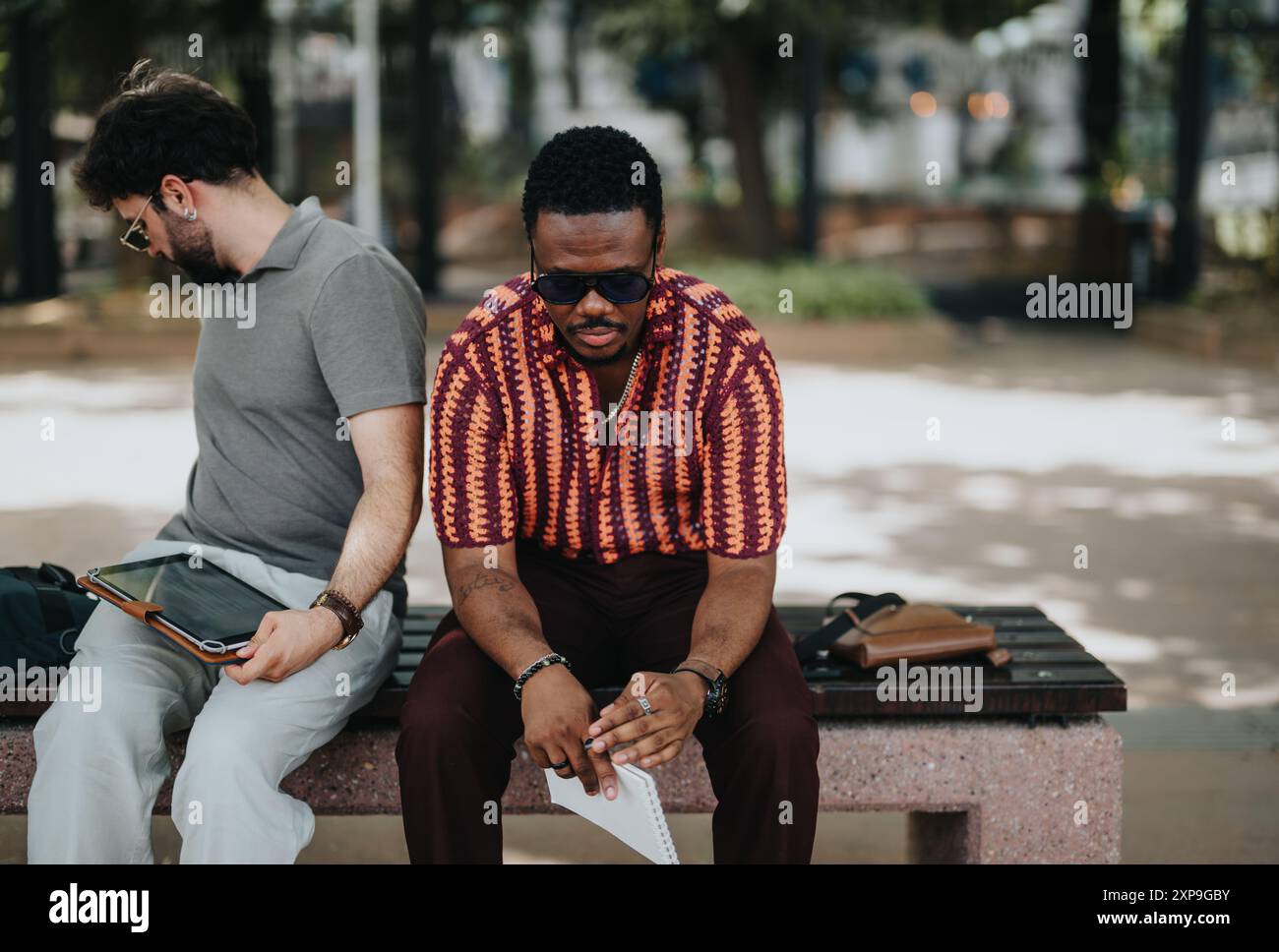 Deux hommes assis sur un banc utilisant des appareils numériques dans un parc extérieur Banque D'Images