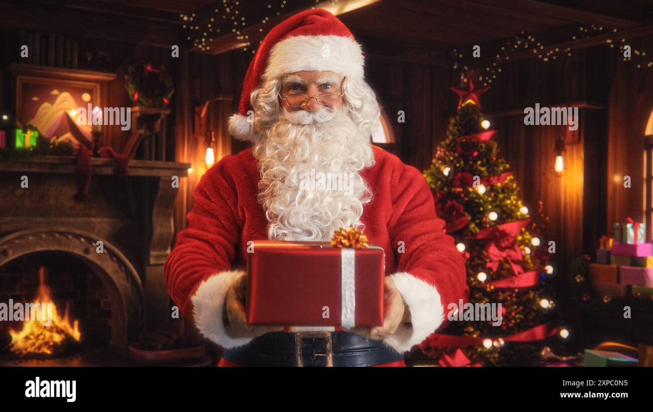 Joyeux Père Noël debout dans une chambre décorée magique, offrant un cadeau rouge magnifiquement enveloppé. Père Noël donnant des cadeaux aux enfants. Concept de Noël et de la célébration des vacances d'hiver du nouvel an Banque D'Images