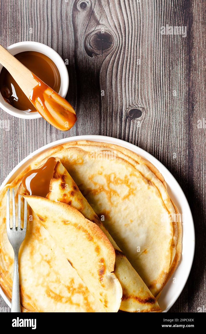 Crêpe Argentine remplie de dulce de leche et un bol de dulce de leche sur fond de bois. Banque D'Images