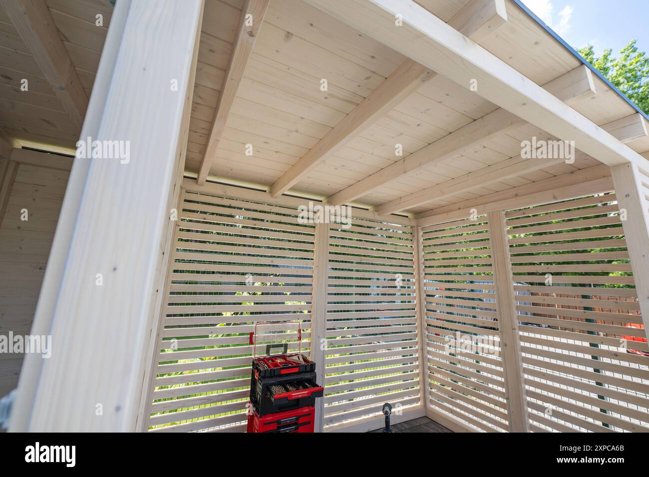 L'intérieur d'un gazebo en bois présente des murs à lattes et la lumière naturelle filtrant à travers, mettant l'accent sur un espace propre et ouvert. Banque D'Images