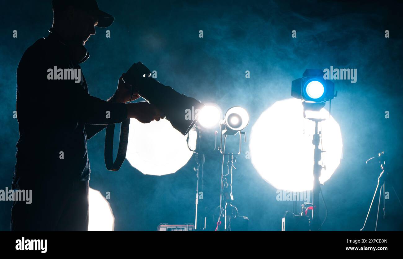 Un photographe en silhouette ajuste son équipement au milieu de lumières vives et de fumée lors d'une séance de studio nocturne. Banque D'Images