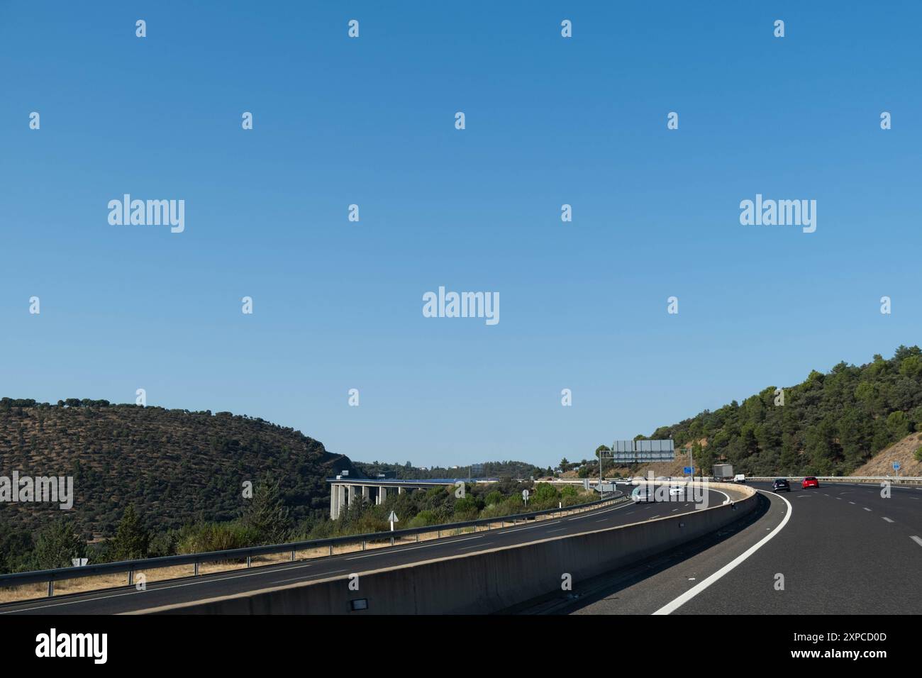 Vue panoramique d'une immense autoroute courbe avec un grand pont en arrière-plan et voitures circulant en Espagne. La journée est claire et ensoleillée et le ciel est bleu Banque D'Images