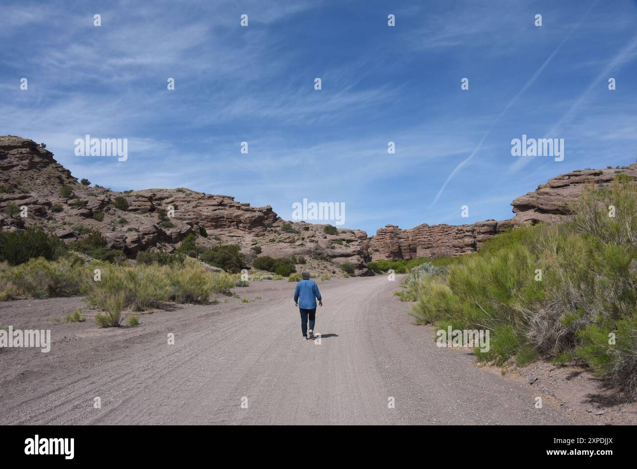 Senior féminine, portant un Jean et une chemise en denim, marche le long du chemin de terre menant au canyon de San Lorenzo au Nouveau-Mexique. Banque D'Images