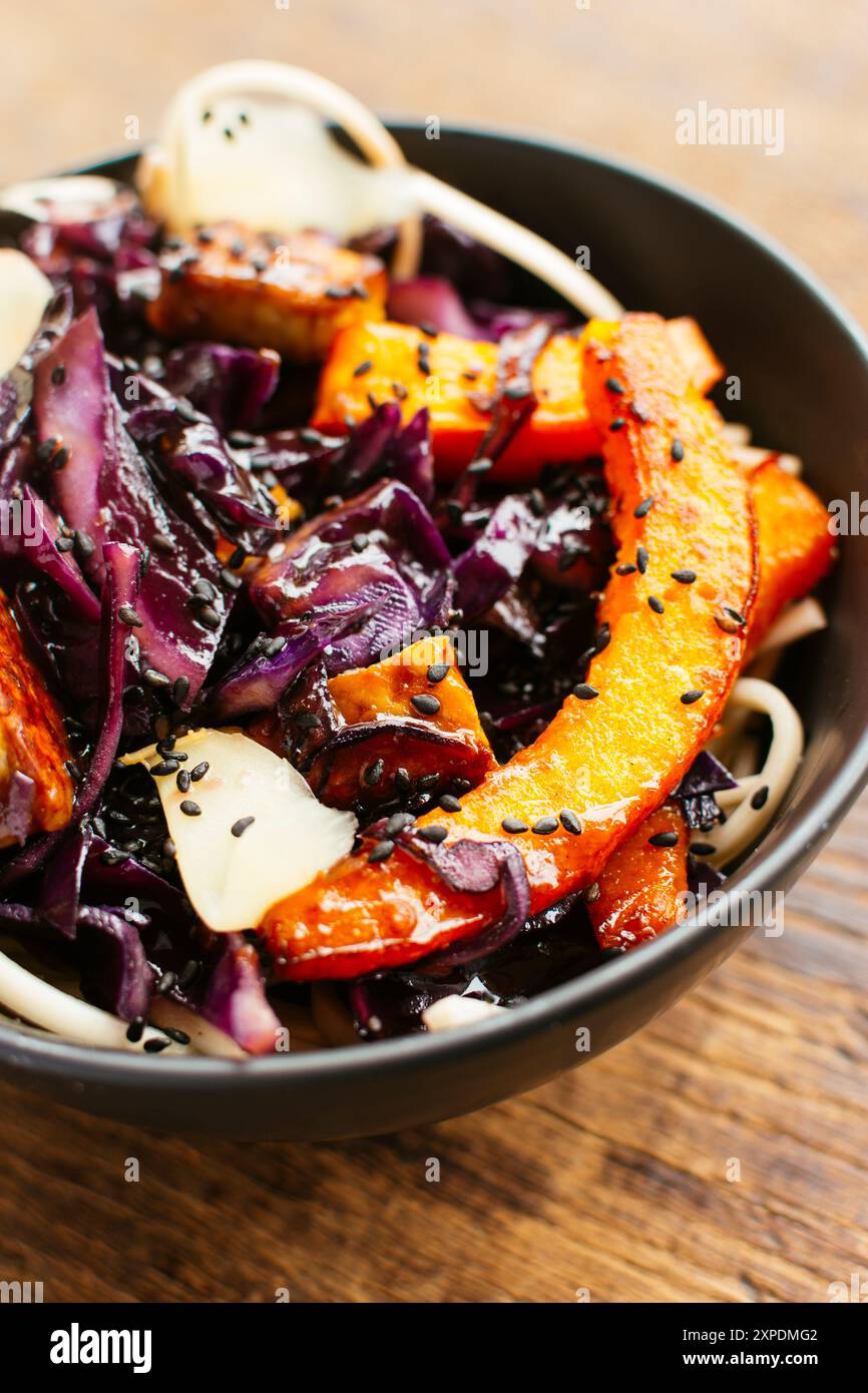 Sauter les légumes d'hiver avec le chou rouge, la courge d'hiver et le tempeh sur les nouilles. Garni de gingembre mariné et de graines de sésame noir. Banque D'Images