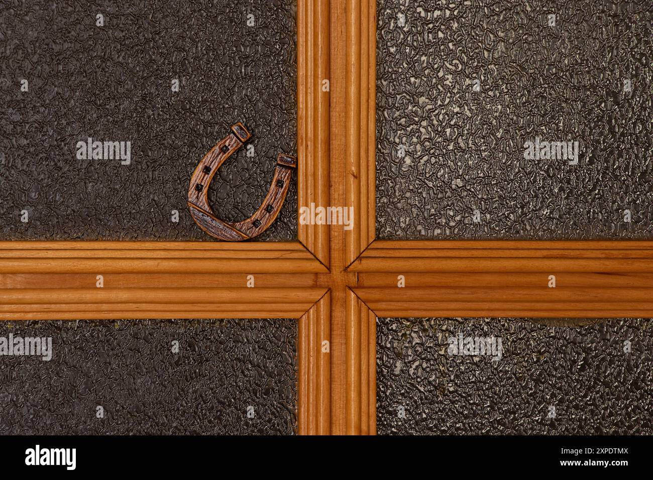 Un petit fer à cheval en bois se dresse sur une porte intérieure en verre dans un appartement, symbole de bonne chance Banque D'Images