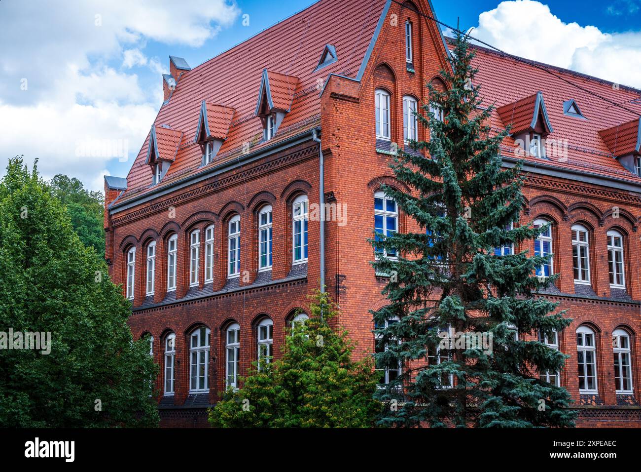 Bâtiment historique en briques rouges entouré d'arbres verdoyants par une journée nuageuse Banque D'Images