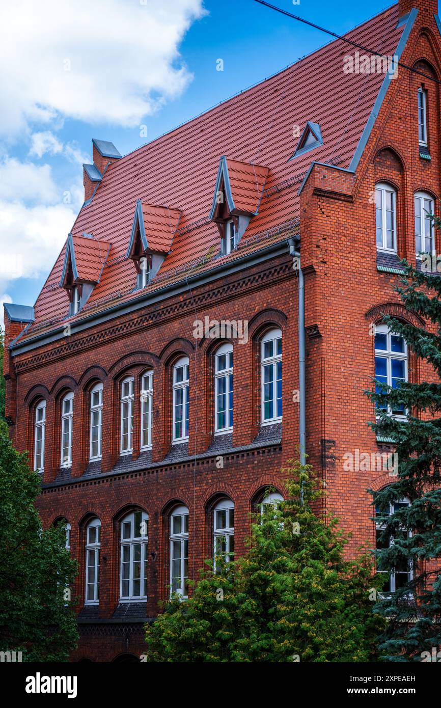 Bâtiment historique en brique avec toit rouge entouré d'arbres sous un ciel bleu Banque D'Images