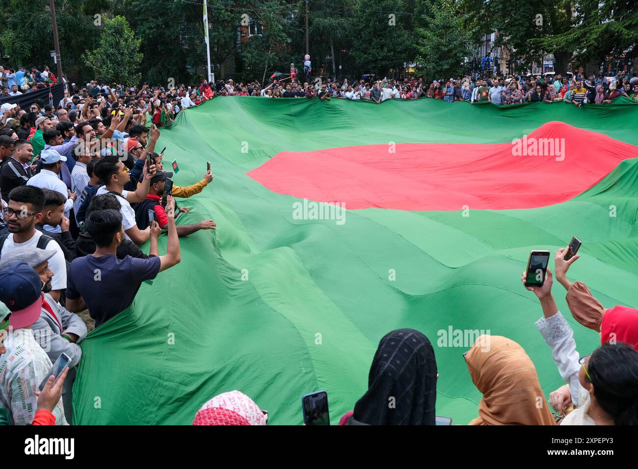 Londres, Royaume-Uni, 5 août 2024. La communauté anglo-bangladaise a célébré la nouvelle de la démission du premier ministre Sheikh Hasina, dans le parc Altab Ali, à l'est de Londres. Des foules entourent un drapeau national géant du Bangladesh. Les protestations étudiantes dans ce pays sud-asiatique contre les quotas d'emplois dans la fonction publique pour ceux qui ont participé à la guerre de libération de 1971 ont conduit à une désatisfaction croissante de la direction de M.S. Hasina. Crédit : onzième heure photographie/Alamy Live News Banque D'Images