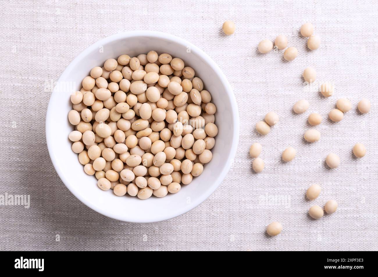 Graines de soja séchées, aussi graines de soja ou graines de soja dans un bol blanc sur tissu de lin. Graines entières et crues de légumineuses et oléagineuses Glycine max. Banque D'Images