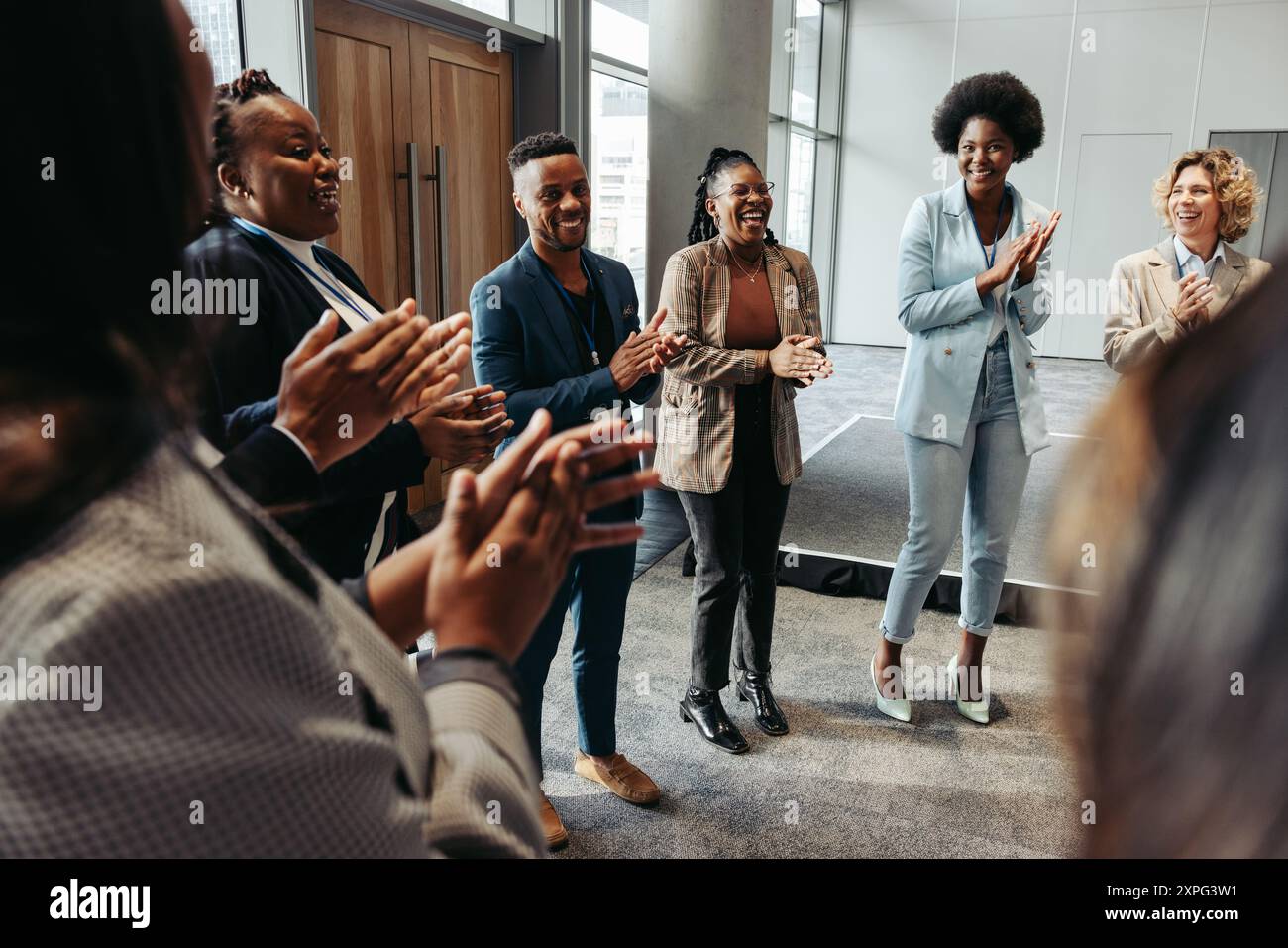 Groupe diversifié de personnes debout en cercle, applaudissant et souriant pendant un séminaire. L’atmosphère est positive et collaborative. Banque D'Images