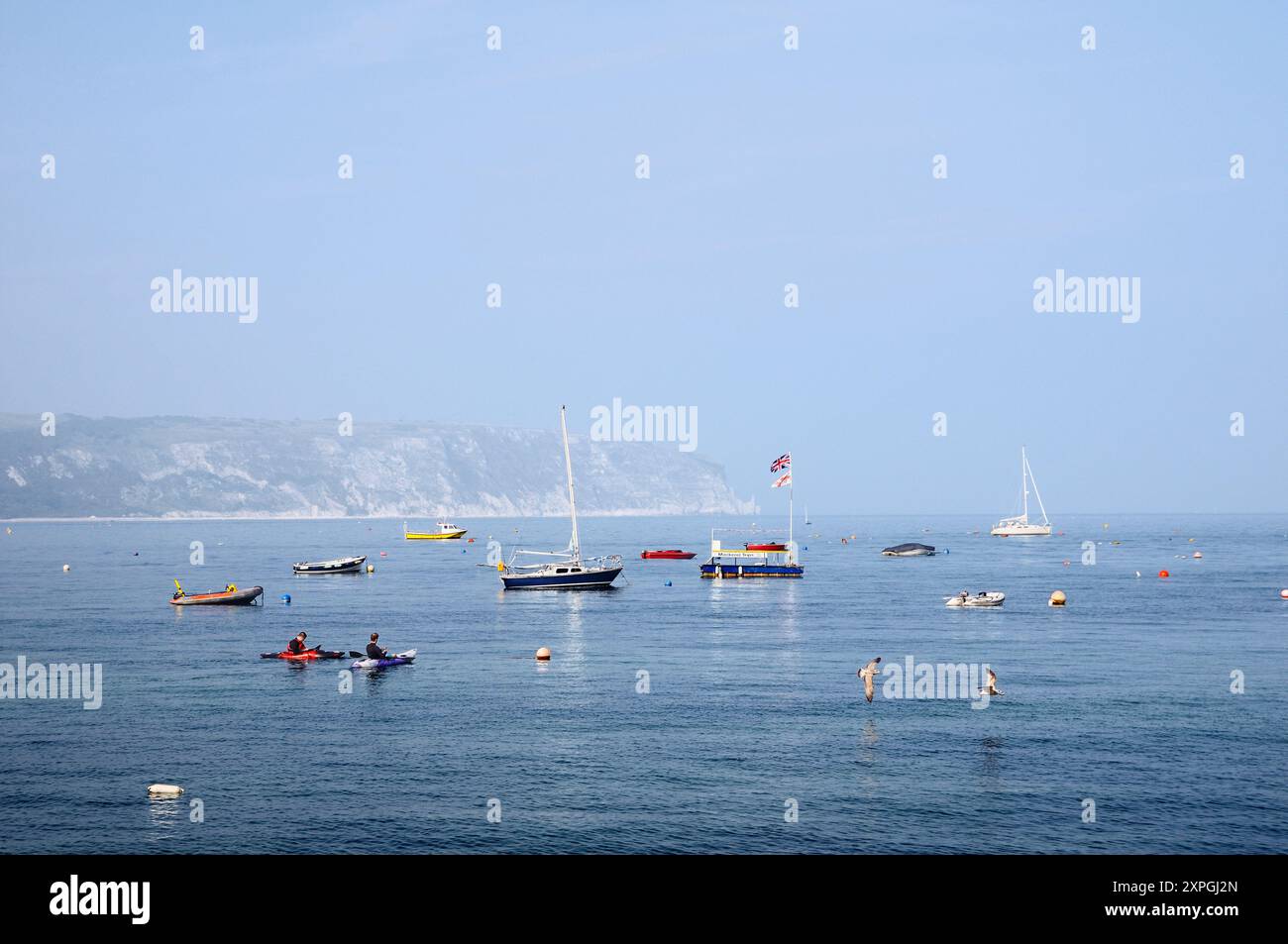 Bateaux amarrés dans la baie de Swanage par un matin d'été ensoleillé et brumeux avec des falaises de craie de Ballard Down et Ballard point Behind, Jurassic Coast, Dorset England UK Banque D'Images