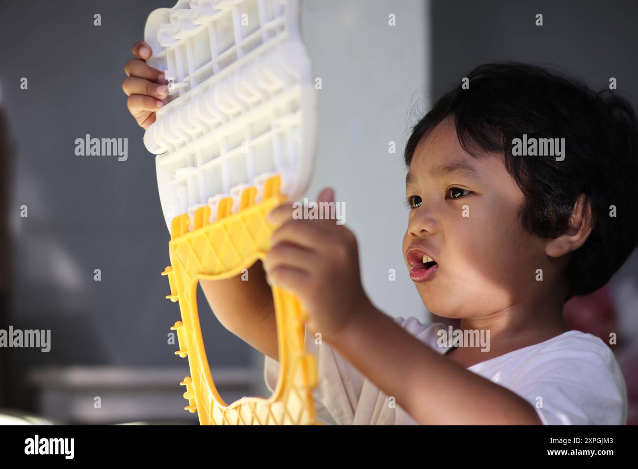 Un jeune garçon profondément concentré, engagé avec un jouet sous un doux éclairage du soleil matinal Banque D'Images