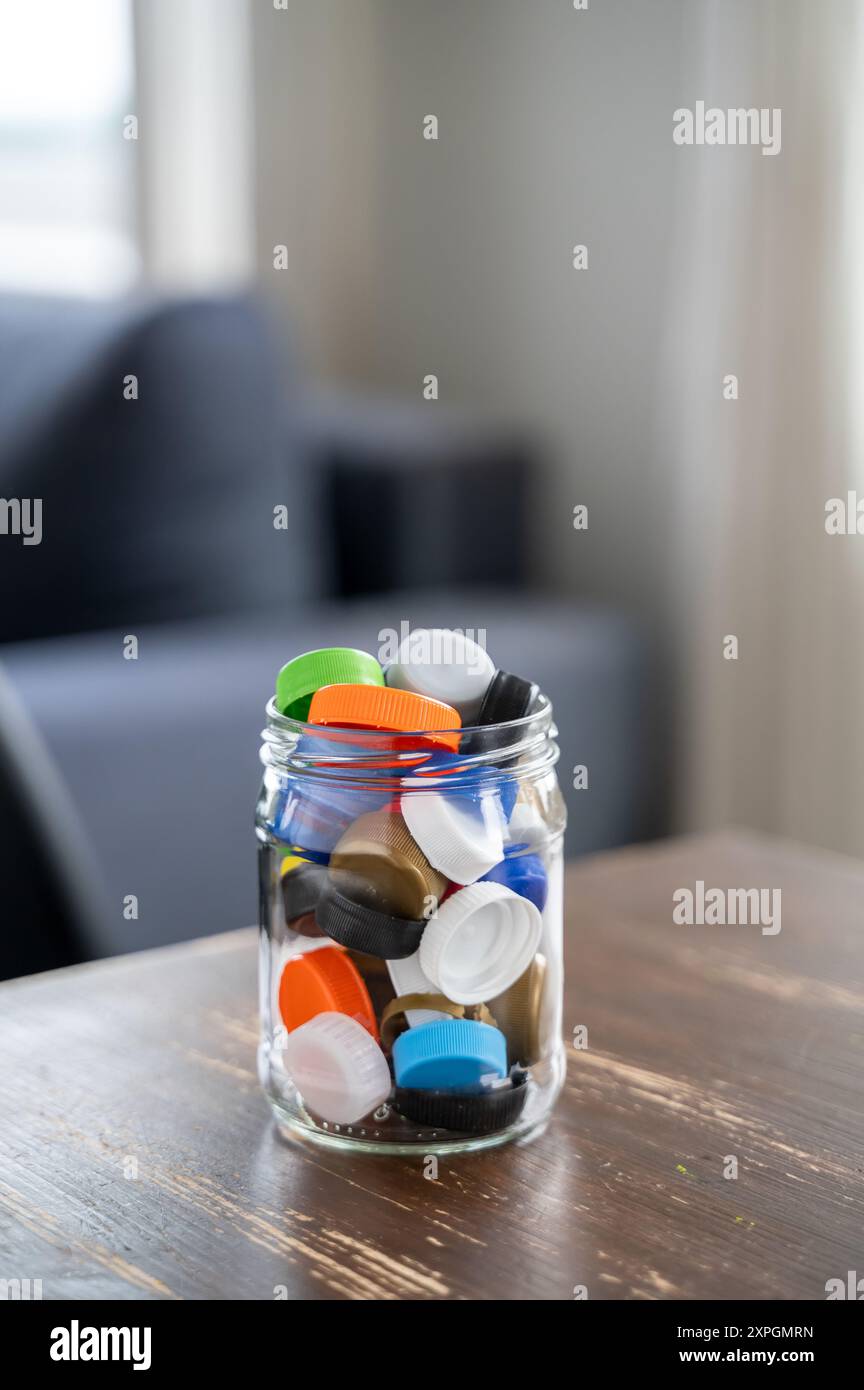 Pot en verre se trouve sur une table en bois, remplie de bouchons de bouteille en plastique coloré. Les bouchons sont collectés pour être recyclés Banque D'Images