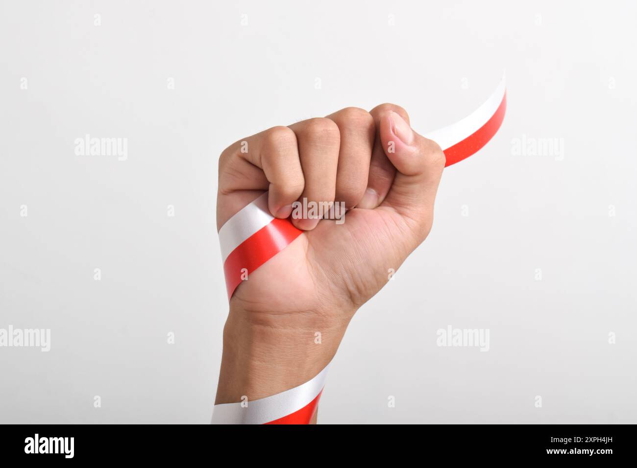 Poing d'homme avec ruban rouge et blanc comme symbole du drapeau indonésien, isolé sur fond blanc. Concept du jour de l'indépendance indonésienne, le 17 août. c Banque D'Images