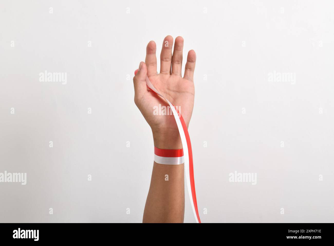 Main tendue avec ruban rouge et blanc comme symbole du drapeau indonésien, isolé sur fond blanc. Concept du jour de l'indépendance indonésienne 17 août. Banque D'Images