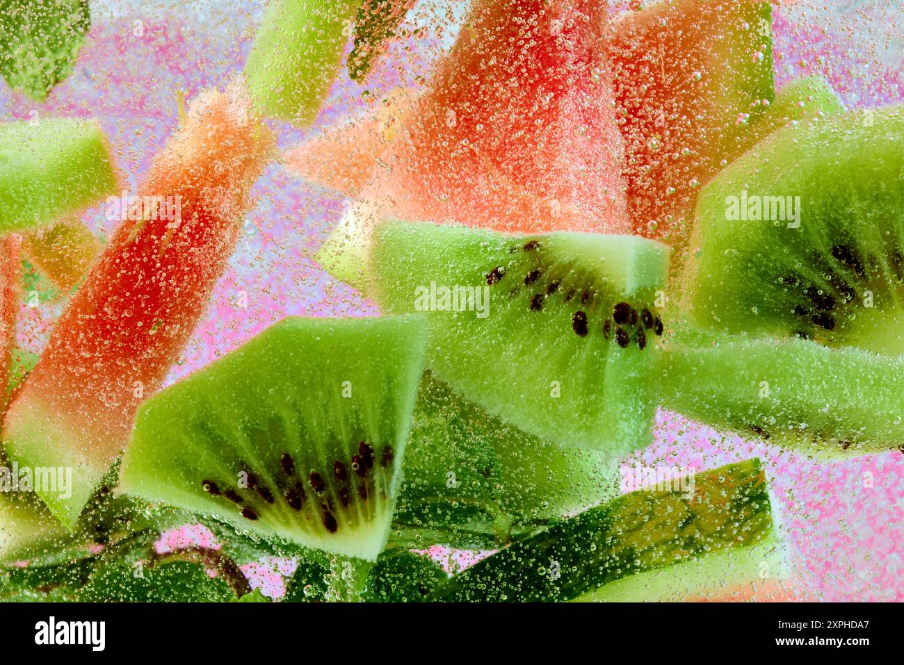 Tranches de pastèque et kiwi flottent avec des feuilles vertes, entourées de bulles sur fond rose pastel. Papier peint texturé. Banque D'Images