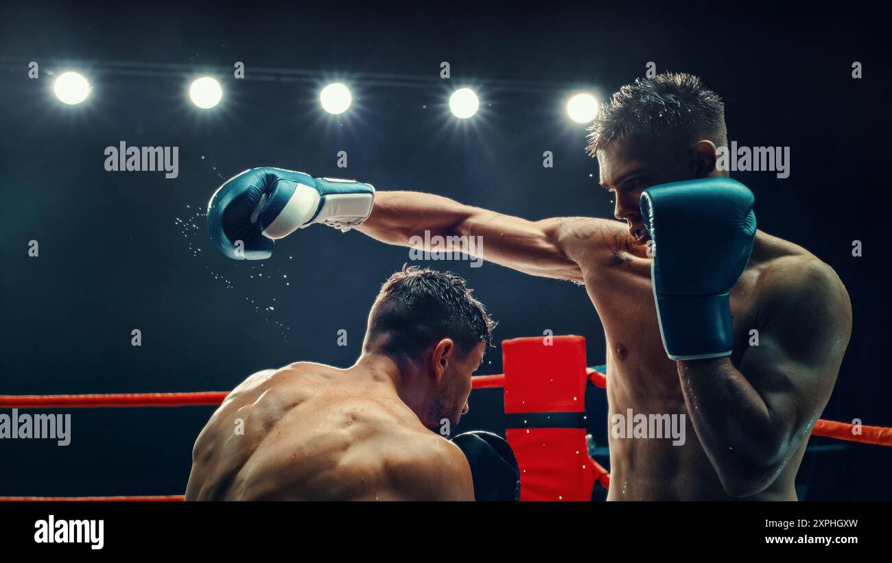 Deux boxers masculins dans un match électrisant, l'un délivrant un puissant punch sous des lumières brillantes. L'intensité et l'énergie brute du combat sont capturées, la sueur s'envole de leur corps. Championnat de boxe Banque D'Images