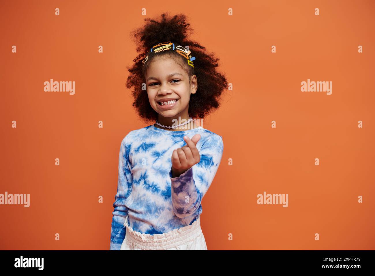 Une jeune fille afro-américaine avec des cheveux bouclés et des pinces à cheveux sourit à la caméra tout en portant une chemise bleue teinte par cravate. Banque D'Images