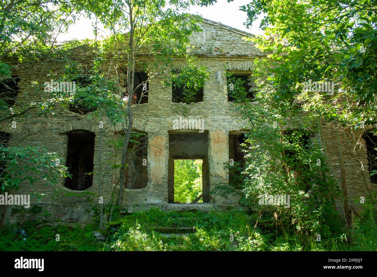 Bâtiment en pierre abandonné envahi de feuillage vert un jour ensoleillé Banque D'Images