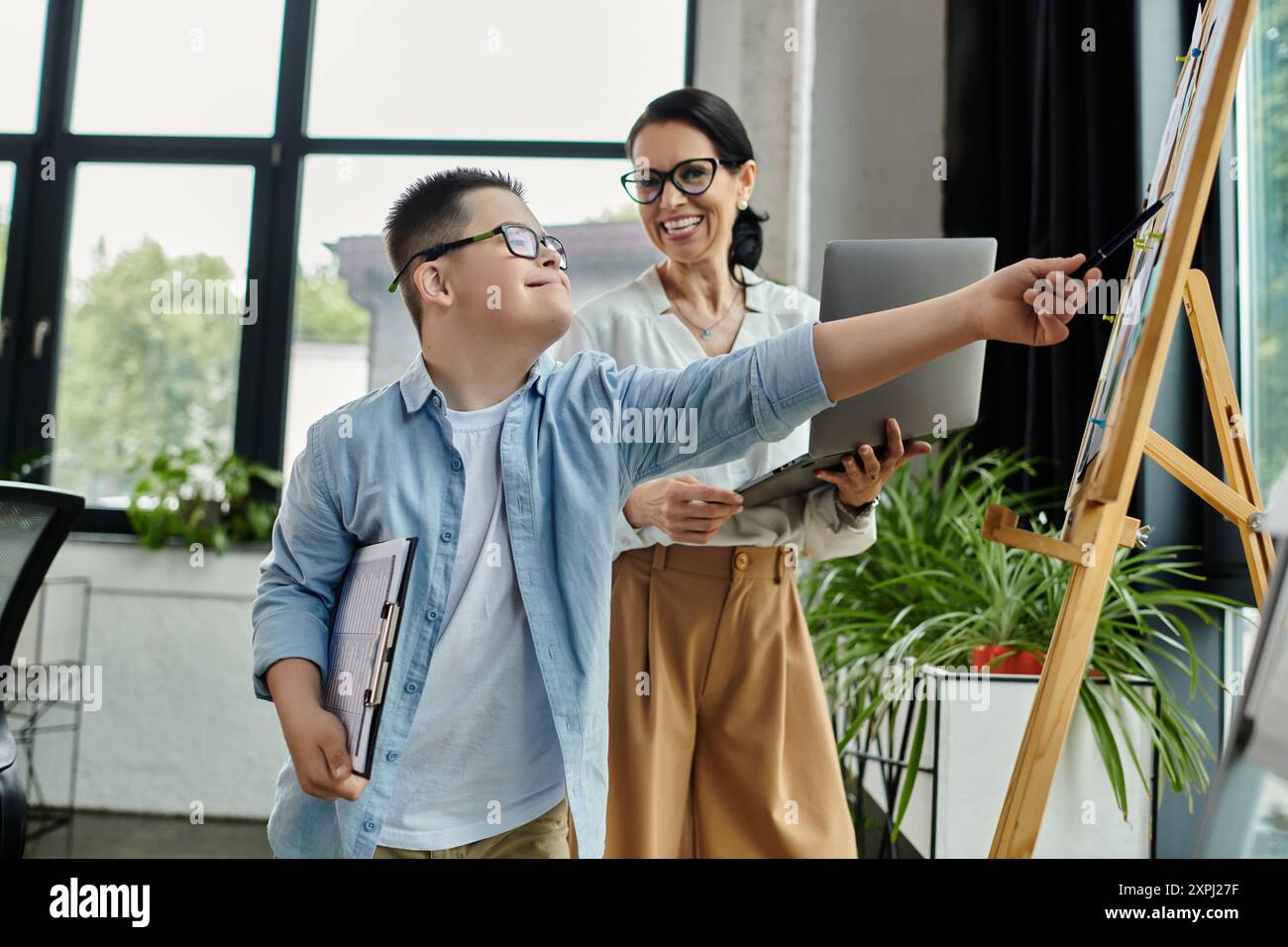 Une mère et son fils atteints du syndrome de Down travaillent ensemble dans un bureau, mettant en valeur l’inclusivité et la diversité. Banque D'Images