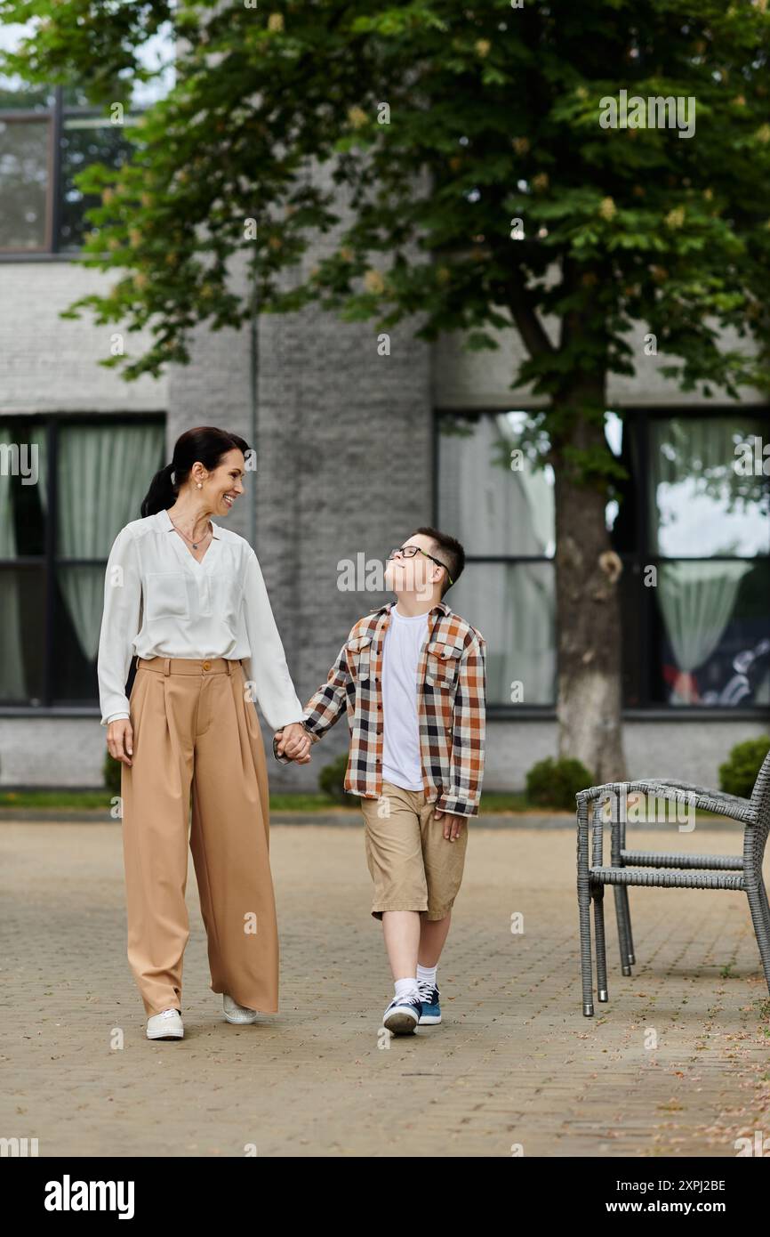 Une mère marche main dans la main avec son fils, atteint du syndrome de Down, près d'un immeuble de bureaux. Banque D'Images