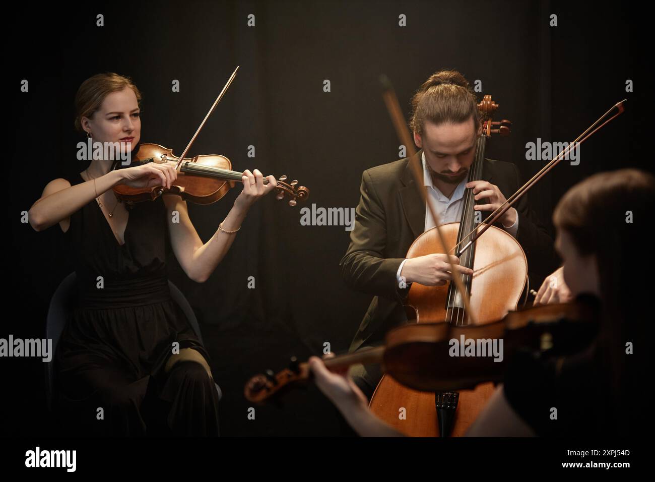 Musiciens professionnels à cordes, femmes et hommes, jouant du violon et du violoncelle avec quatuor de chambre contre des rideaux noirs Banque D'Images