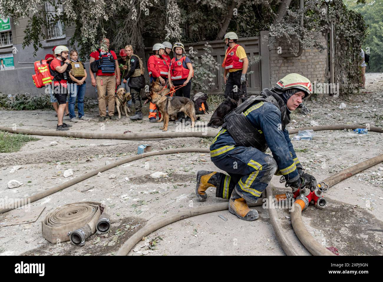 Kharkiv, Ukraine. 06 août 2024. Un pompier libère de l'eau à travers une pompe pendant que les chiens de secours et leurs maîtres attendent, en attendant les ordres. La grève russe sur Kharkiv le mardi 6 août 2024 a fait 8 blessés et infligé de graves dégâts à 15 bâtiments, dont des bureaux, une polyclinique, une université et 25 voitures. (VX photo/ Vudi Xhymshiti). Crédit : VX Pictures/Alamy Live News crédit : VX Pictures/Alamy Live News Banque D'Images