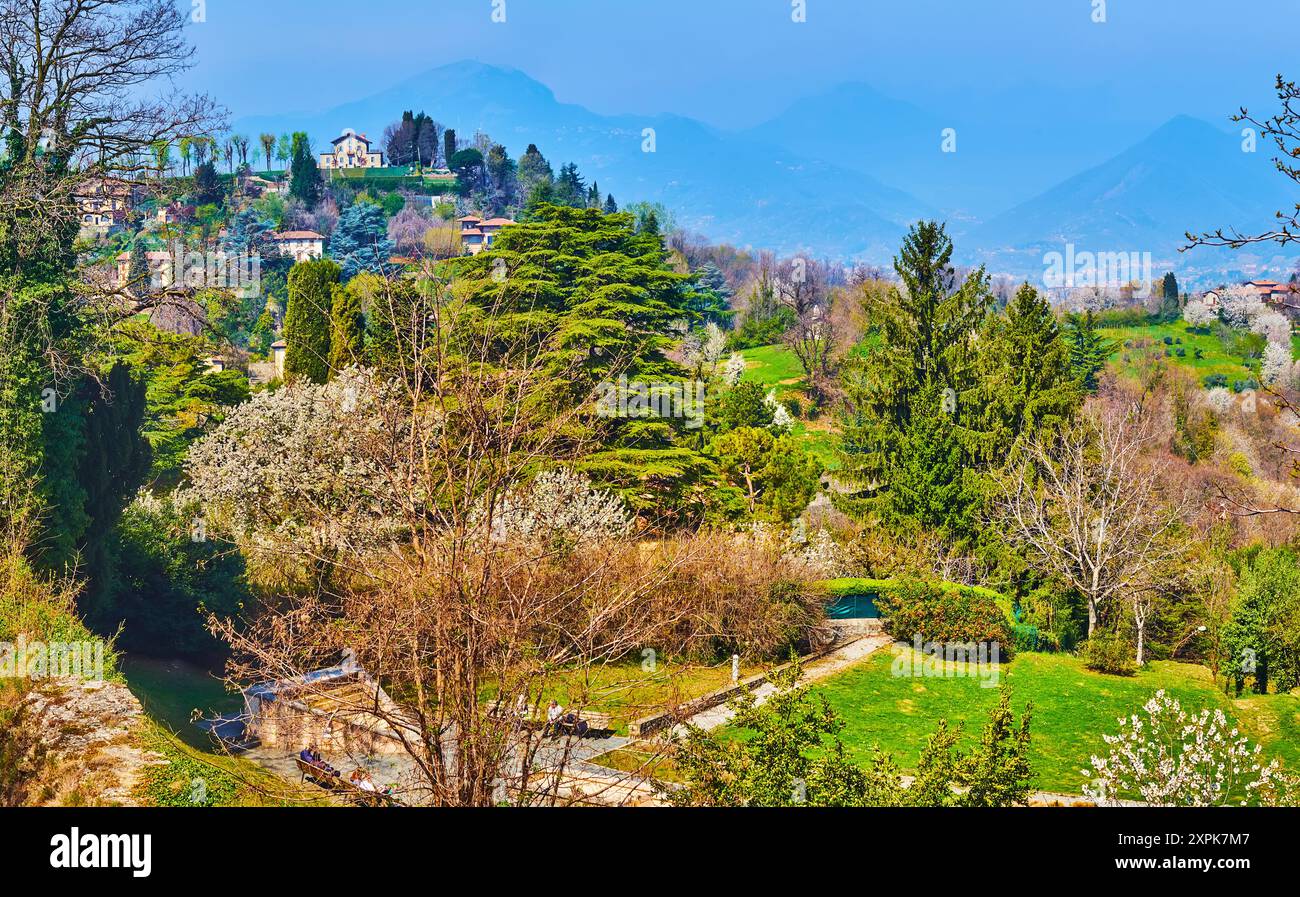 Monte Bastia avec des maisons vintage et des jardins verdoyants derrière les épinettes et les arbres de printemps en fleurs sur la pente de la colline de San Vigilio, Bergame, Italie Banque D'Images