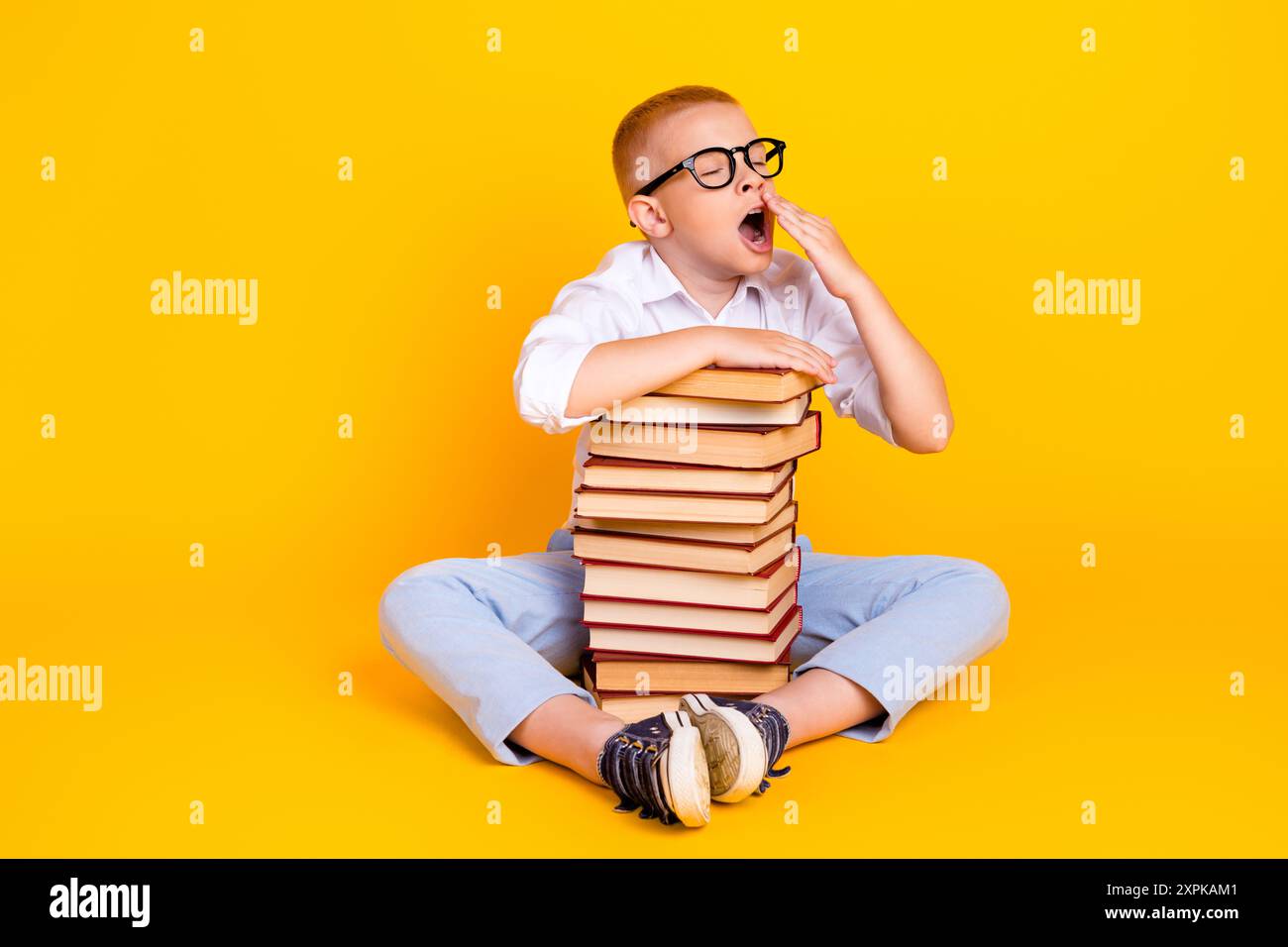 Photo de intelligent mignon fatigué Sleepy Boy Wear chemise blanche lire beaucoup de livre isolé sur fond de couleur jaune Banque D'Images