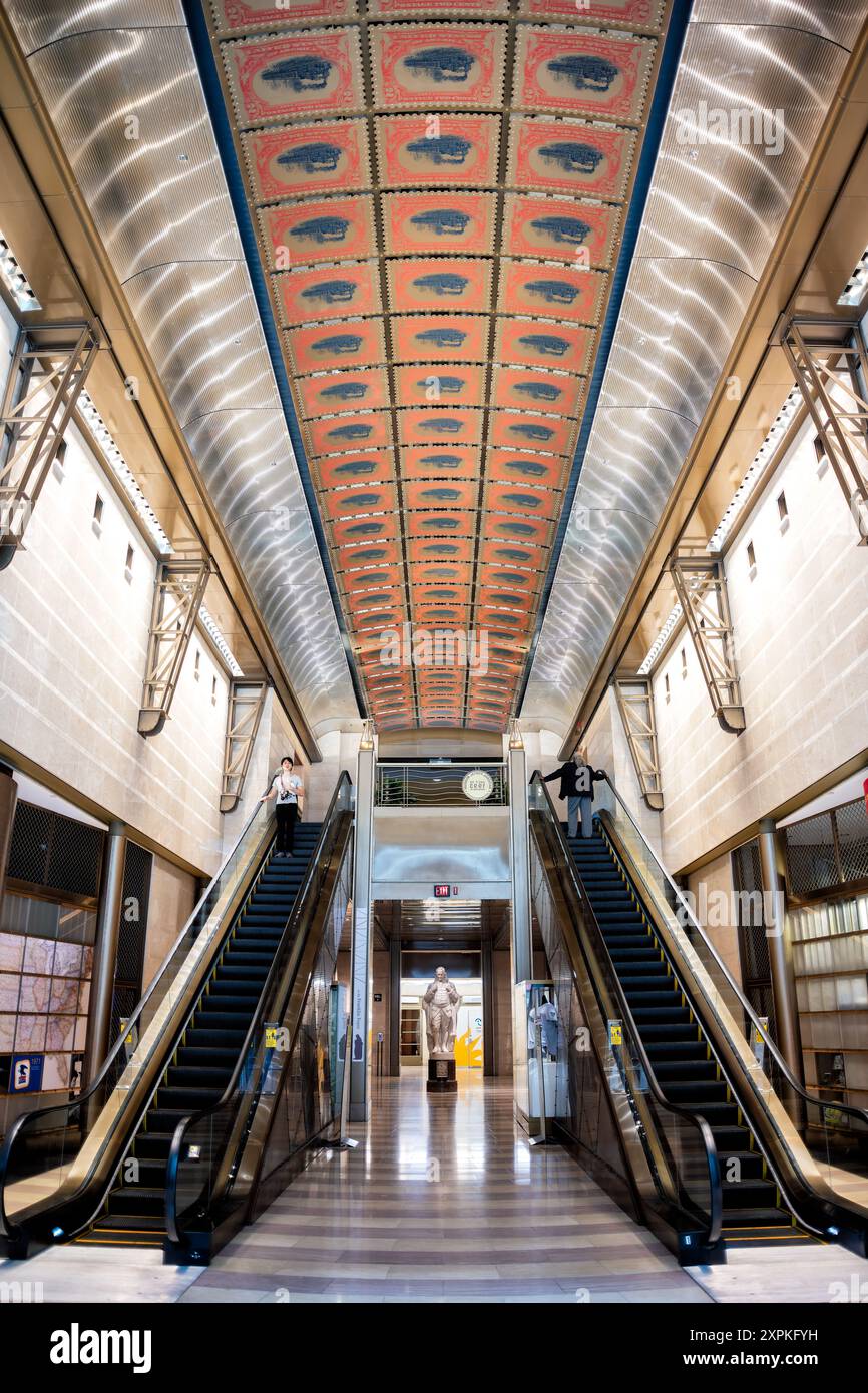 Musée national de la poste atrium et escalators Washington DC // WASHINGTON DC — L'atrium principal et les escalators au niveau inférieur du musée national de la poste Smithsonian à Washington, DC. Cette vue présente la conception à plusieurs niveaux du musée, avec des escaliers mécaniques permettant un accès facile entre les étages. L'atrium ouvert permet aux visiteurs d'apprécier la grandeur de l'espace et de voir les expositions suspendues sous différents angles. Banque D'Images