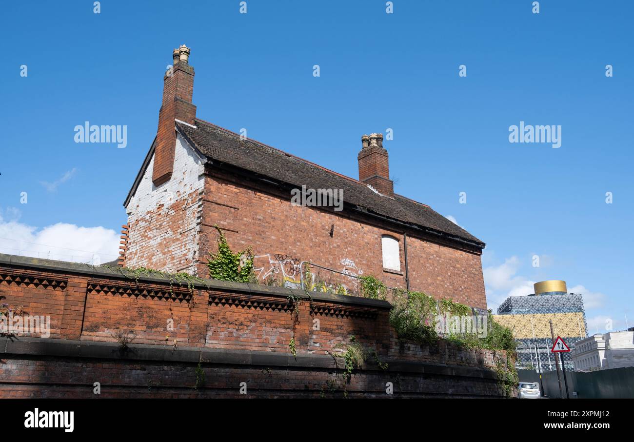 Un vieux bâtiment en briques rouges côté canal se trouve inutilisé dans le centre-ville de Birmingham avec la nouvelle bibliothèque de la ville en arrière-plan montrant un contraste historique. Banque D'Images
