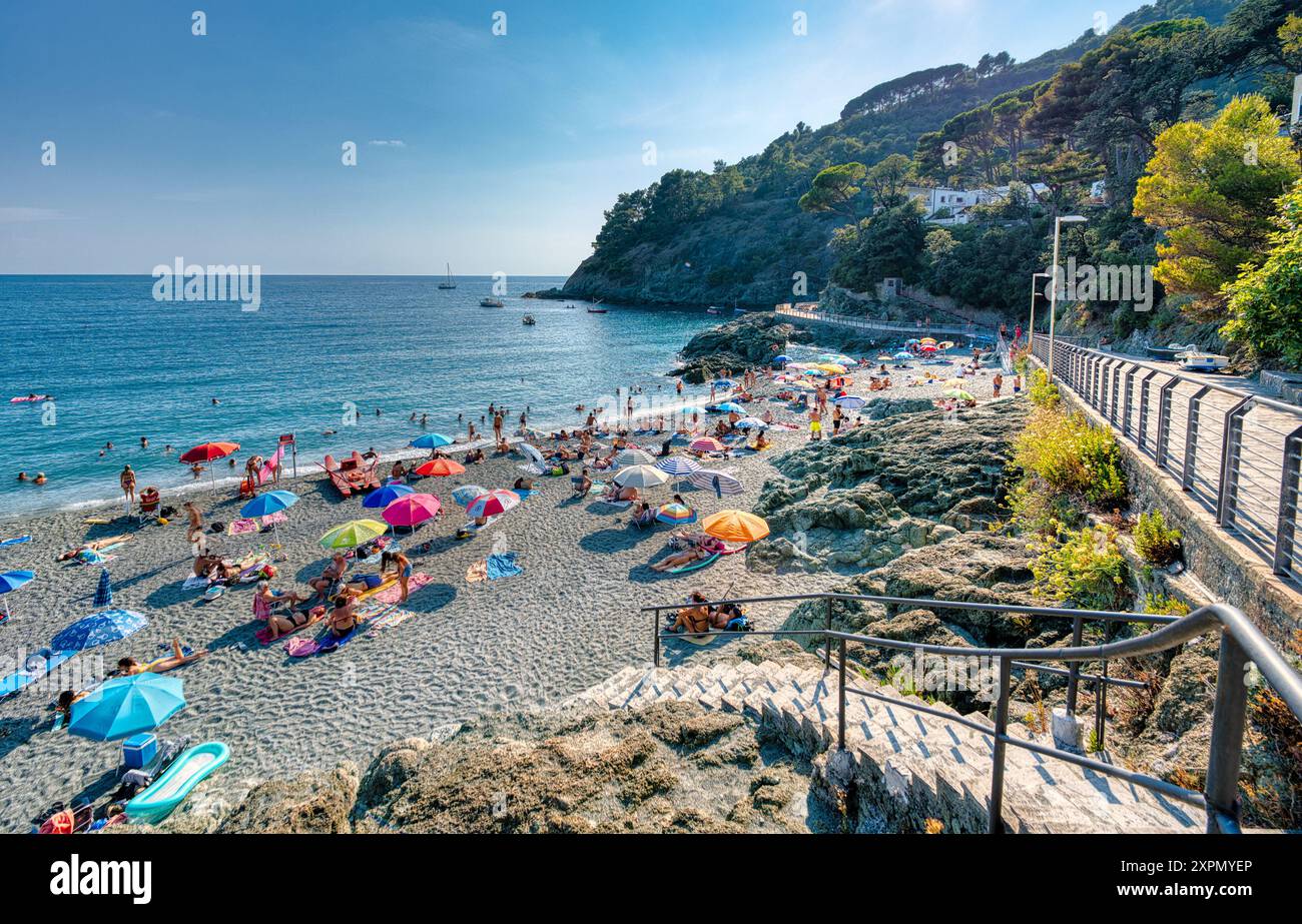 Une plage animée avec des parasols colorés, une mer calme, et une charmante ville à flanc de colline en arrière-plan. Parfait pour une escapade estivale. Banque D'Images