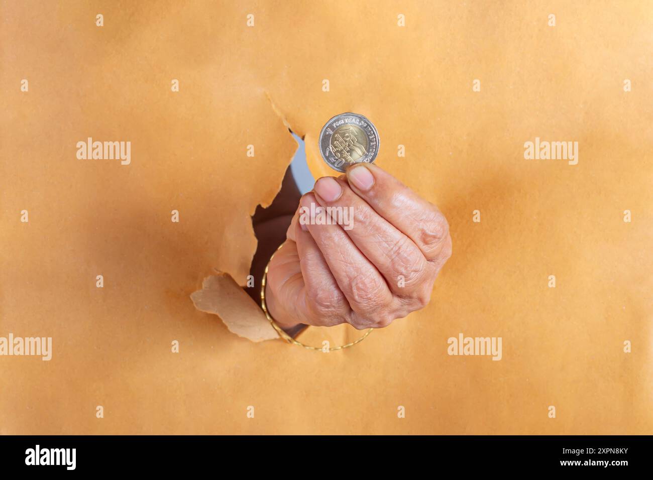 Gros plan de la main de femme senior tenant la pièce indienne de 20 roupies à travers un trou dans le papier brun. Banque D'Images